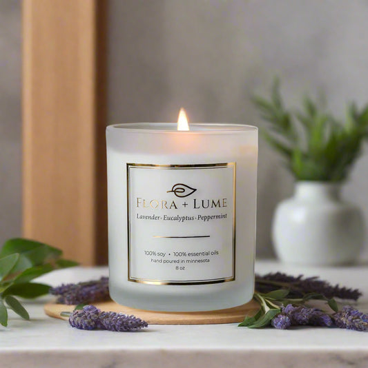 Flora + Lume candle on a reflective surface with a blurred background